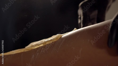 Master of sugaring is applying wax and quickly removing from skin of woman hip. Close-up in a beautician office in beauty shop