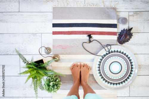 Top view of an unidentified young woman's leg with a beautiful pedicure stand on the rug next to spiritual accessories for yoga candles and karatals on the floor