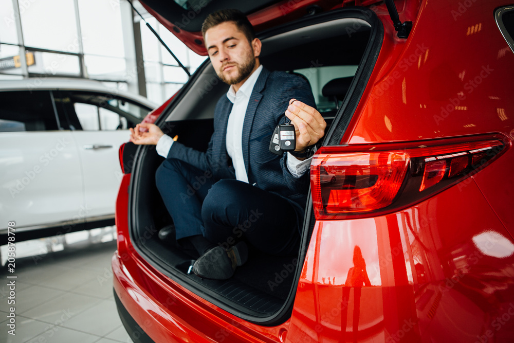 Excited businessman sitting in car. Showing new car key.