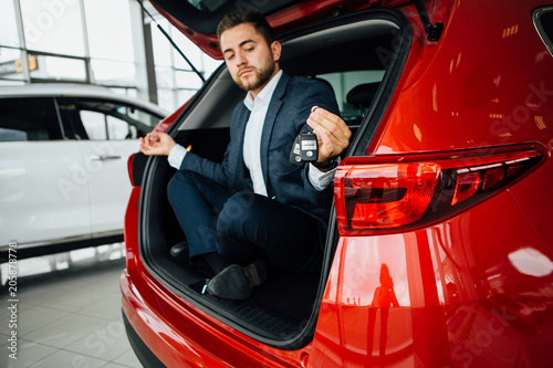 Excited businessman sitting in car. Showing new car key.