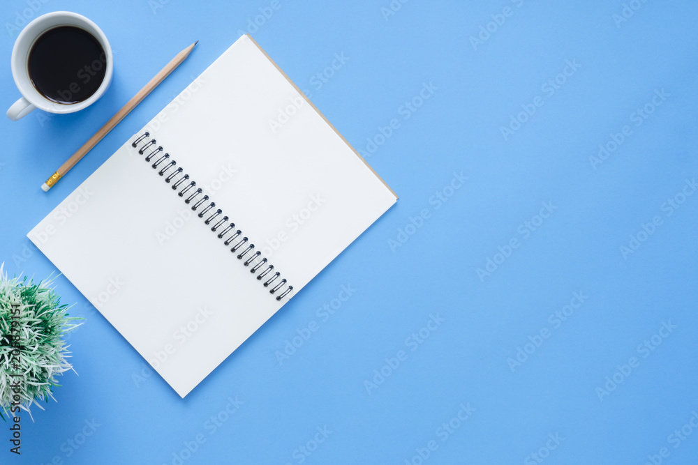 Office desk working space - Flat lay top view mockup of a working space with white blank notebook page, coffee cup on blue pastel background. Pastel blue color background space concept. Office desk working space - Flat lay top view mockup of a working space with white blank notebook page, coffee cup on blue pastel background. Pastel blue color background space concept.