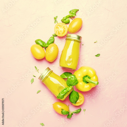 Useful and healthy smoothie or juice from yellow tomatoes and bell peppers with green basil and oregano in glass bottles, pink background, top view