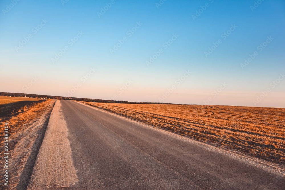 Road near a field at sunset in a clear gradient sky
