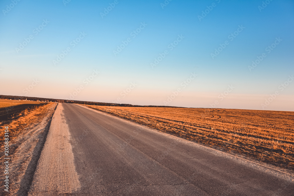 Road near a field at sunset in a clear gradient sky Road near a field at sunset in a clear gradient sky