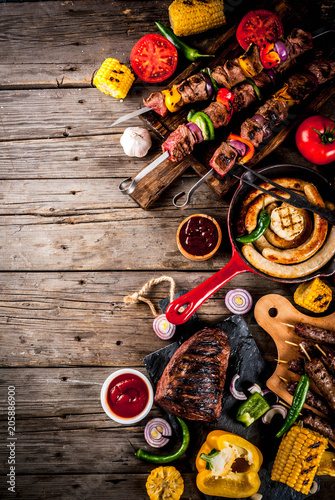 Assortment various barbecue food grill meat, bbq party fest - shish kebab, sausages, grilled meat fillet, fresh vegetables, sauces, spices, on old wooden rustic table, above copy space