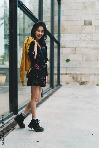Young fashion designer form Asia standing beside the office building. Traveler female visiting interesting city sights during vacation. Student girl in trendy outfit standing on a street.