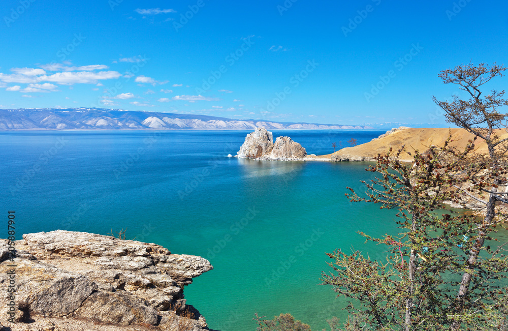 Baikal Lake on a sunny May day. A view of the natural landmark - Shamanka Rock from the coast of Olkhon Island. On the larch trees on the shore begins to appear young green needles