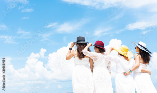 Group of four women in white dress and wearing hat standing along the beach with blue sky background. Summer and vacation conceept. photo