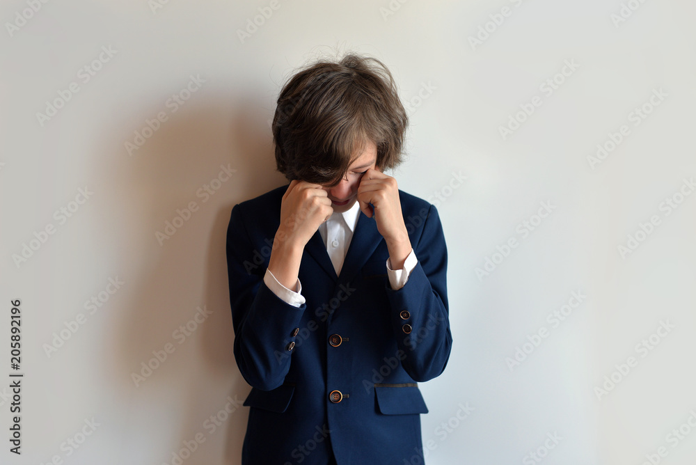 The schoolboy is in despair. The schoolboy is crying. Schoolboy in uniform with closed face on a white background The schoolboy is in despair. The schoolboy is crying. Schoolboy in uniform with closed face on a white background