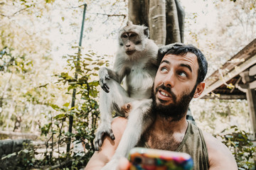 .Young handsome man taking himself some pictures with a cute monckey in the monckey forest in Ubud, Bali. Lifestyle. Travel photography