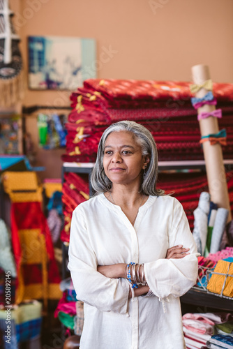 Mature fabric shop owner standing among her colorful textiles