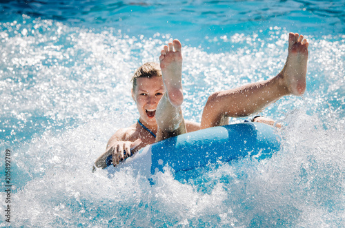 Funny girl taking a fast water ride on a float splashing water. Summer vacation with water park concept.