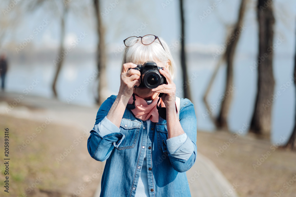 My favourite activity. Inspired mature woman taking pictures while walking in the park