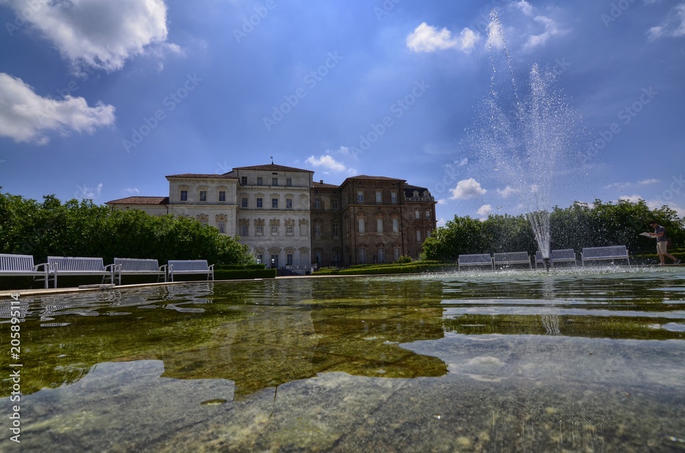 Obraz premium Venaria reale, Piedmont region, Italy. June 2017. The facade of the palace, on the side of the gardens, is reflected on the fountain's water mirror. Tourists explore the magnificent park.