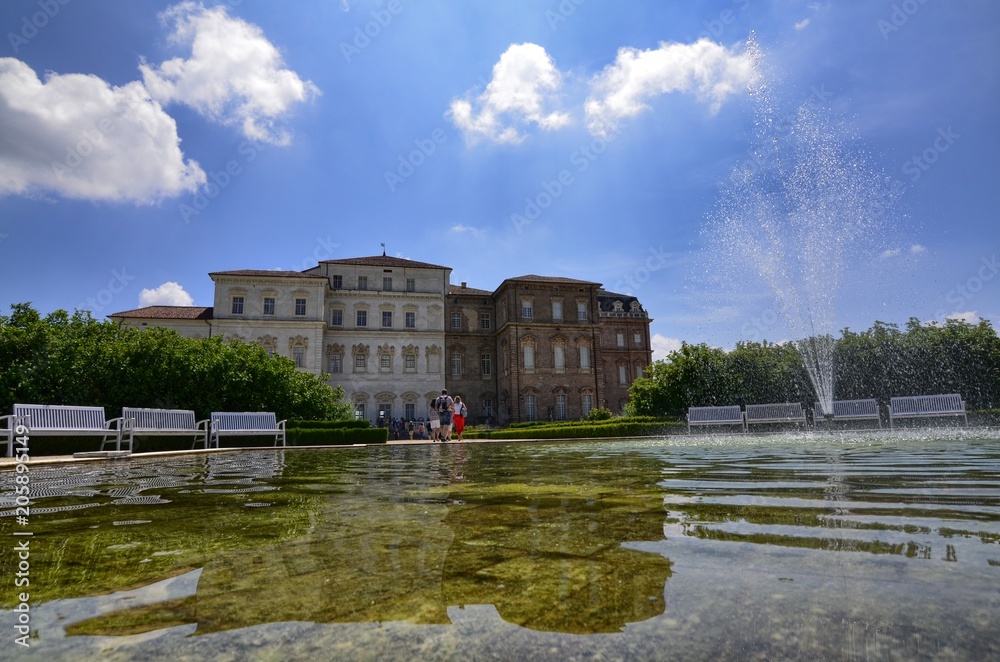 Venaria reale, Piedmont region, Italy. June 2017. The facade of the palace, on the side of the gardens, is reflected on the fountain's water mirror. Tourists explore the magnificent park.