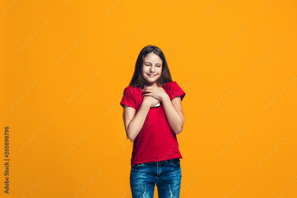 The happy teen girl standing and smiling against orange background. The happy teen girl standing and smiling against orange background.