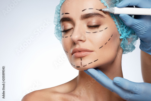 Hands in blue gloves drawing lines on woman's face