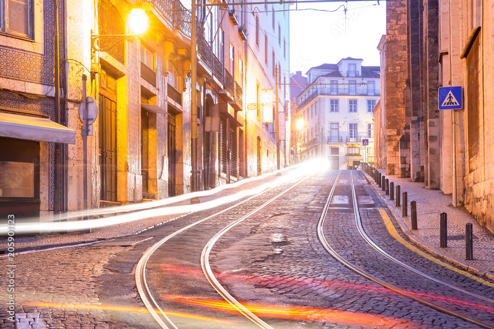 Cozy empty street with tram tracks and light tracks in Alfama, the oldest district of the Old Town in the morning, Lisbon, Portugal Cozy empty street with tram tracks and light tracks in Alfama, the oldest district of the Old Town in the morning, Lisbon, Portugal