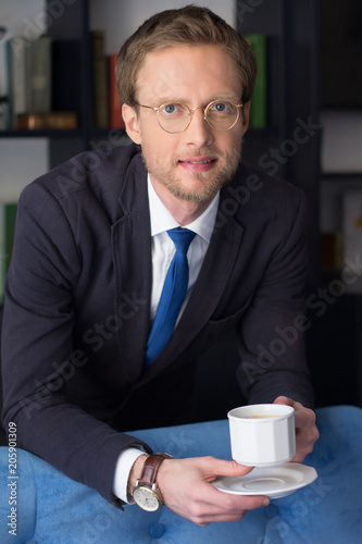 Businessman having cup of tasty coffee and posing on camera. Coffee break concept. © Svyatoslav Lypynskyy