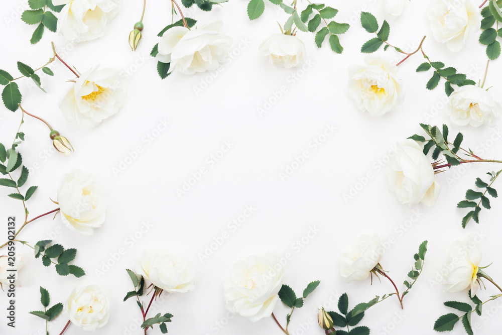 Beautiful white rose flowers and green leaves on table top view. Wedding frame in flat lay styling.