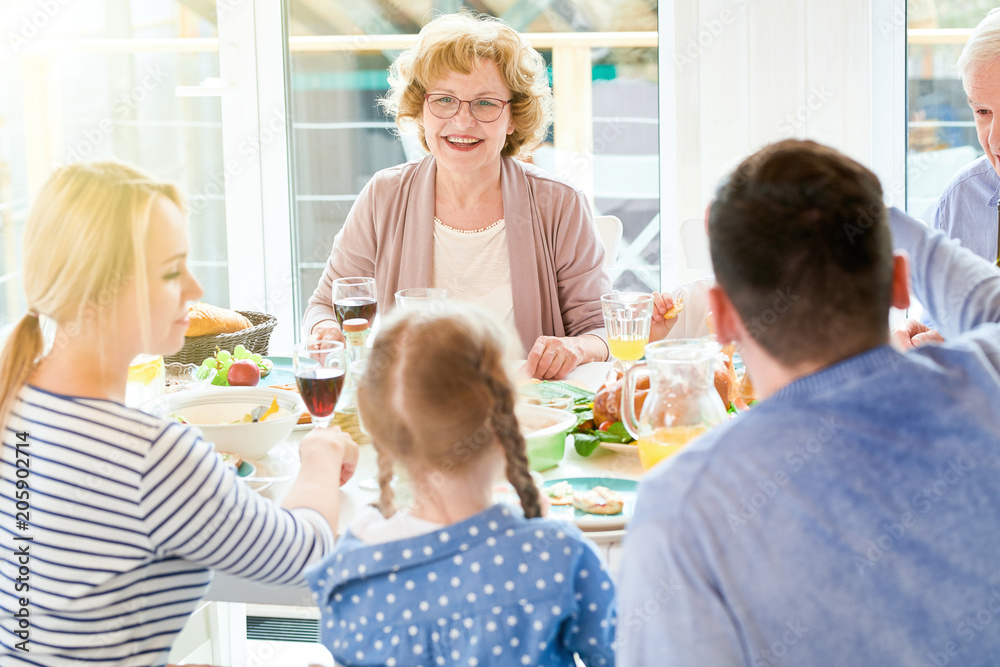 Portrait of happy family enjoying dinner together sitting round festive table with delicious dishes focus on mature woman smiling during holiday celebration in modern sunlit apartment, copy space Portrait of happy family enjoying dinner together sitting round festive table with delicious dishes focus on mature woman smiling during holiday celebration in modern sunlit apartment, copy space