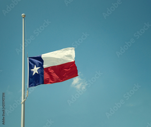 State flag of Texas flying at half-mast or half-staff on a flagpole. Blue sky background with copy space. Vintage tone.