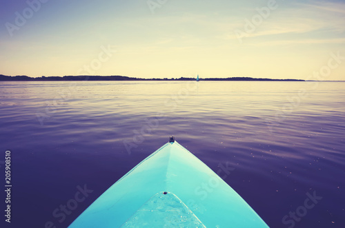 Fototapeta Naklejka Na Ścianę i Meble -  Bow of a kayak on a still lake at sunset, color toned picture, selective focus. 