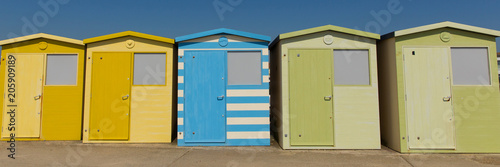 Beach huts in a row with green blue and yellow colours and blue sky panoramic view