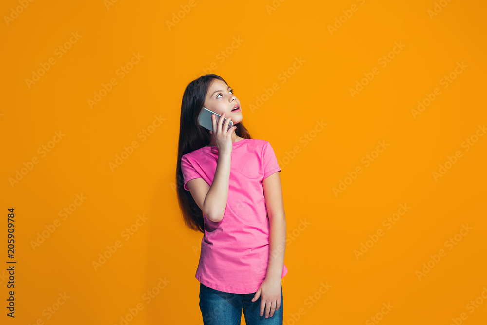 The happy teen girl standing and smiling against orange background. The happy teen girl standing and smiling against orange background.