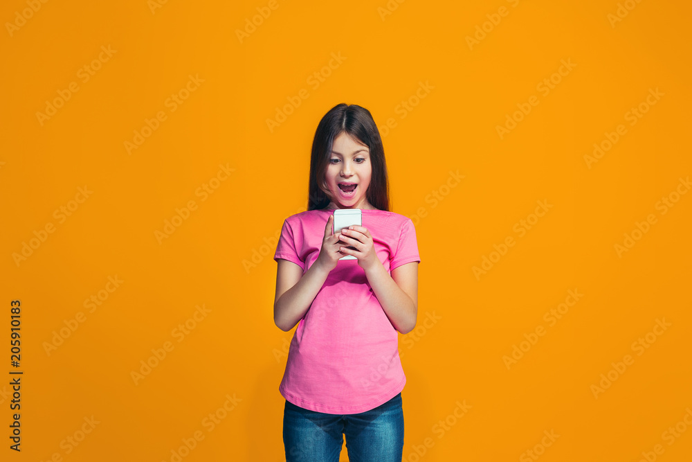 The happy teen girl standing and smiling against orange background. The happy teen girl standing and smiling against orange background.