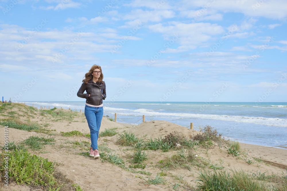 Woman standing at the beach in casual jeans and leather jacket