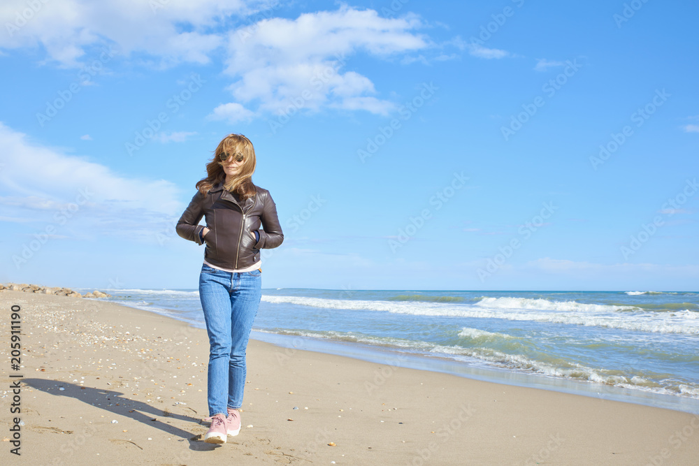 Woman standing at the beach in casual jeans and leather jacket Woman standing at the beach in casual jeans and leather jacket