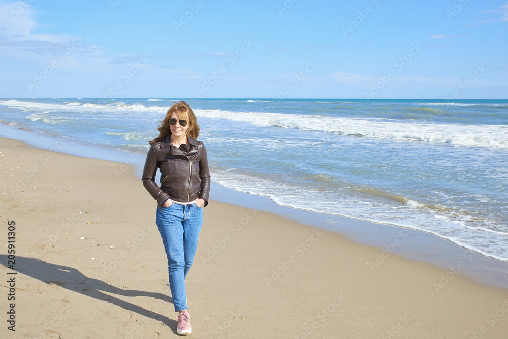 Woman standing at the beach in casual jeans and leather jacket Woman standing at the beach in casual jeans and leather jacket