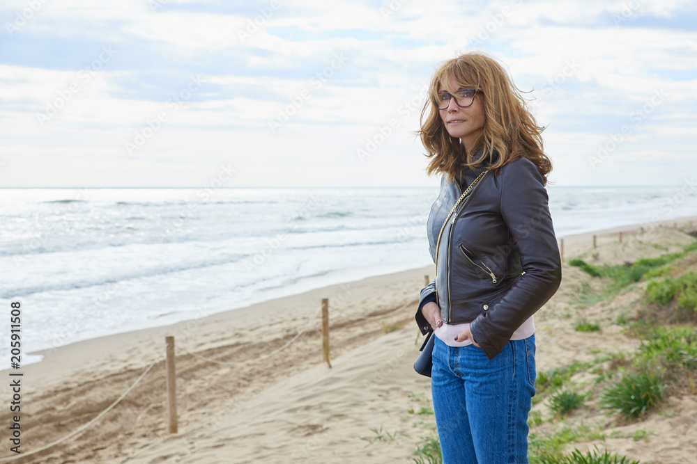 Woman standing at the beach in casual jeans and leather jacket Woman standing at the beach in casual jeans and leather jacket