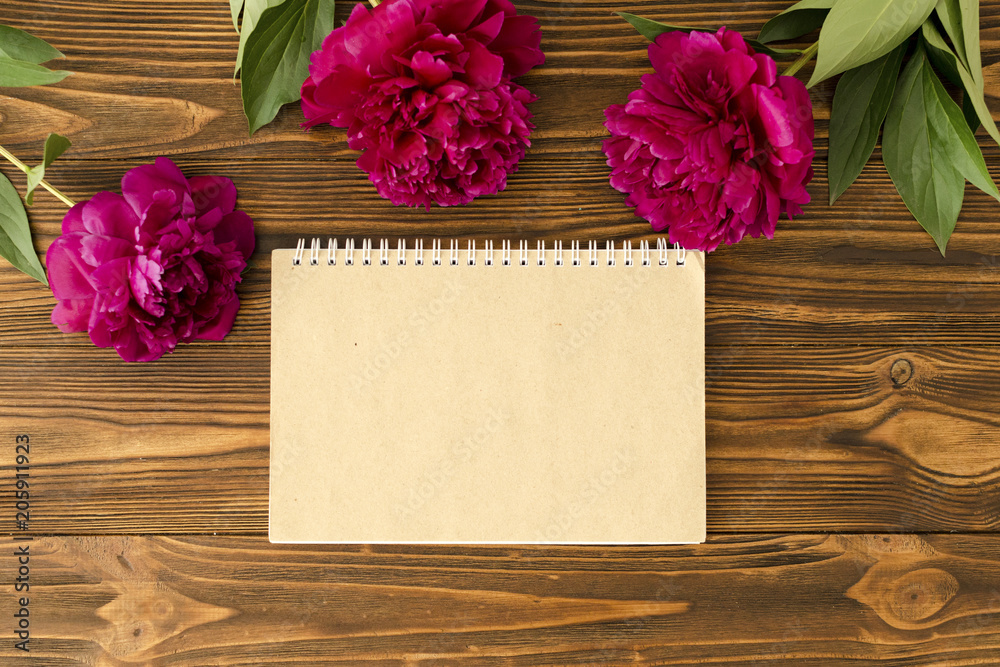 peonies, empty notepad craft paper sheet on wooden background