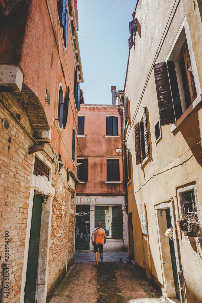 tourist with an orange backpack and bandana walks along narrow street in Europe. Italy Venice in summer. The facade of old houses without people and crowds of tourists. Unpublished places in Venice