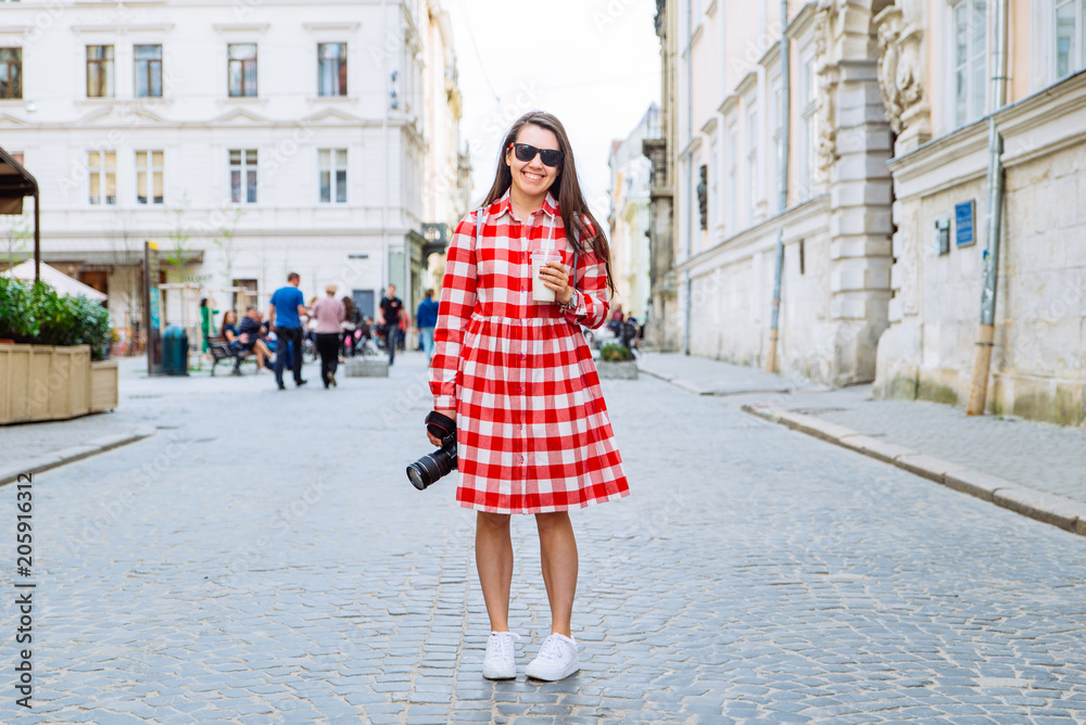 woman walking by city streets with cool drink and camera