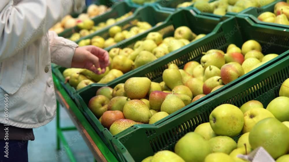 Someone selects pears in the supermarket. Female hand chooses green fruits in the vegetable department at the grocery store. Someone selects pears in the supermarket. Female hand chooses green fruits in the vegetable department at the grocery store.