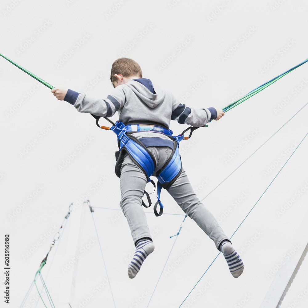 boy teenager jumps high to the sky insured with slings on an entertaining attraction.