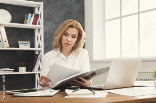 Thoughtful businesswoman reading document at office desktop