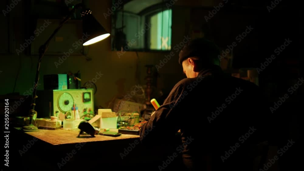 Technician master with soldering iron and analog equipment in dark place with lamp light Technician master with soldering iron and analog equipment in dark place with lamp light