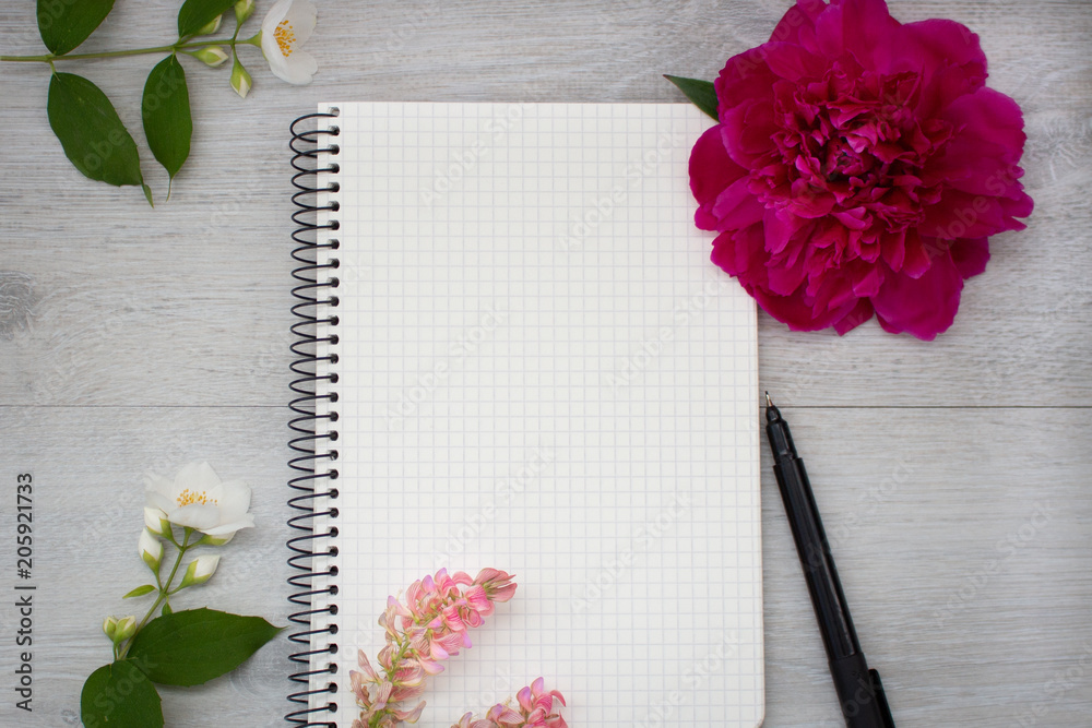 Naklejka premium Open blank notepad, pen, jasmine and peony on the light wooden table. Workplace flat lay