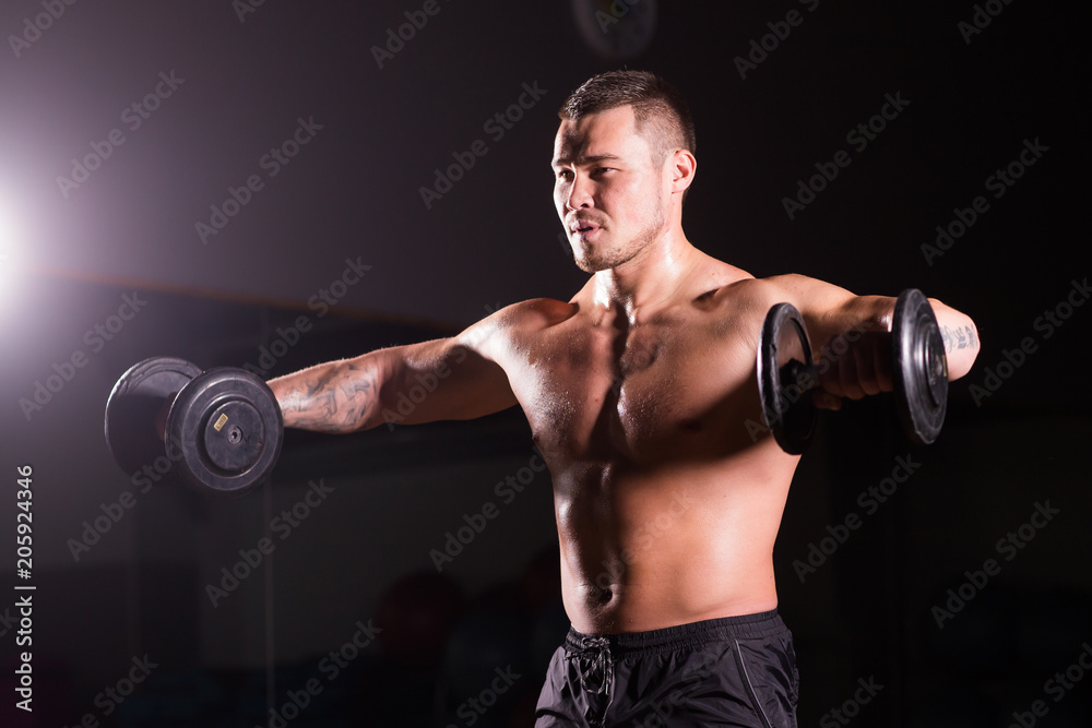 Handsome power athletic man with dumbbell. Strong bodybuilder with six pack, perfect abs, shoulders, biceps, triceps and chest Handsome power athletic man with dumbbell. Strong bodybuilder with six pack, perfect abs, shoulders, biceps, triceps and chest