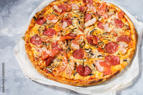 Fresh homemade pizza with pepperoni, ham, cheese and tomato sauce on rustic concrete background.