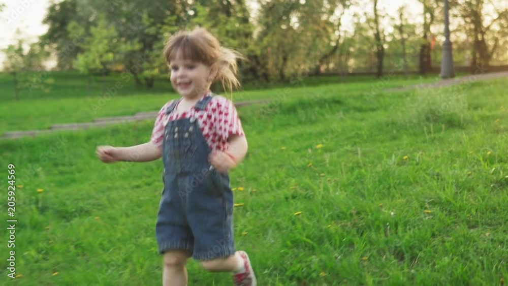 Happy little girl running on green grass at sunset in sunny summer day Happy little girl running on green grass at sunset in sunny summer day