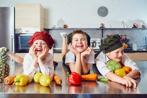 Funny children in the uniform of cooks on the table in vegetables in the kitchen.