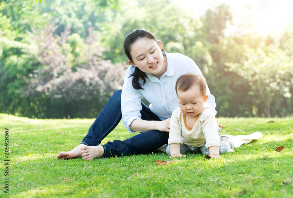 Fototapeta premium Happy mother and baby sitting on meadow in park