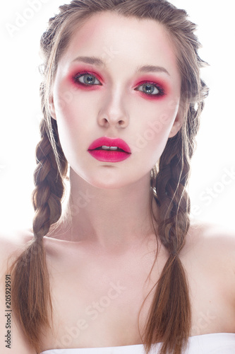 Young girl with bright pink creative make-up. A beautiful model with shining skin and braids. White isolated background. Beauty of the face. Photo is taken in the studio.
