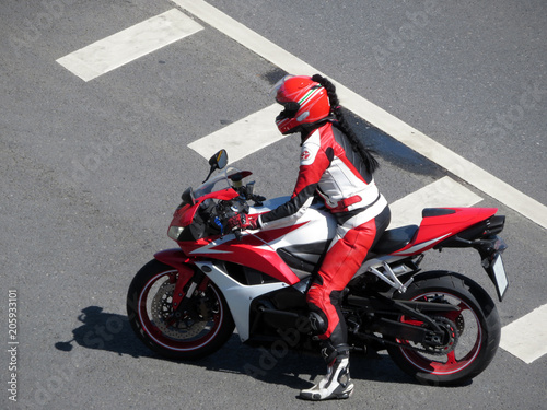 Biker girl in a leather jacket and red helmet on a motorcycle. Young woman driving a motorbike on the road