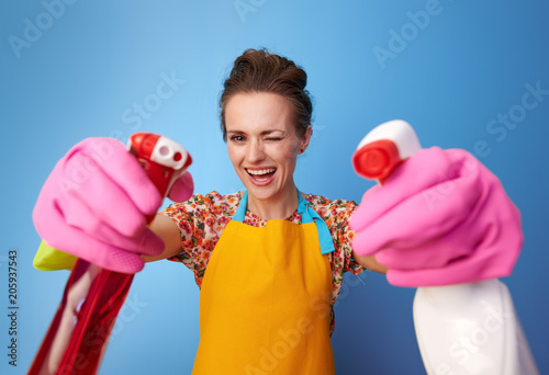 happy woman using bottles of cleaning detergent as guns on blue